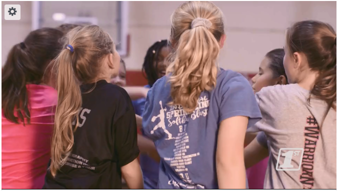 A team of girls are encircled in a huddle as their hands are extended to each other in unity!